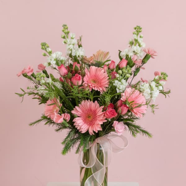 Pink mixed flower bouquet in a clear glass vase with a sheer ribbon