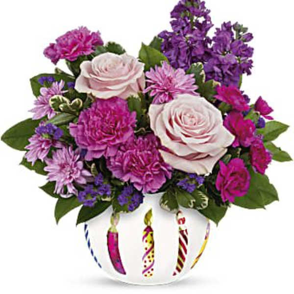 Pink and purple flower arrangement in a white vase with striped candle designs