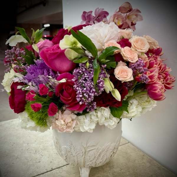 Mixed pink, white, and purple flowers arranged in a white pedestal vase.