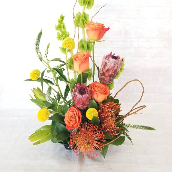 Tall mixed bouquet with orange roses, protea, and yellow accents in a vase