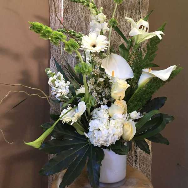 White floral arrangement with calla lilies, roses, and gerbera daisies in a white vase