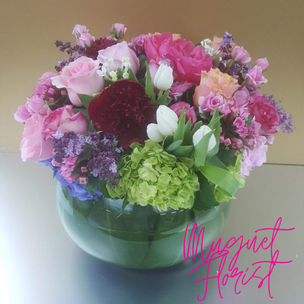 Mixed pink and purple flower arrangement in a round glass vase