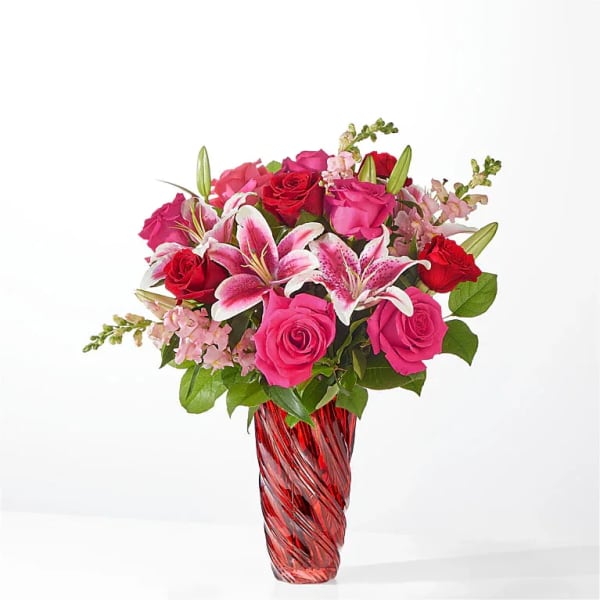 Pink and red roses with lilies in a red glass vase