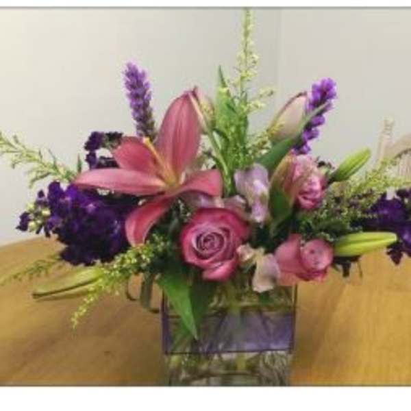 Pink lilies and roses in a glass vase with purple accents