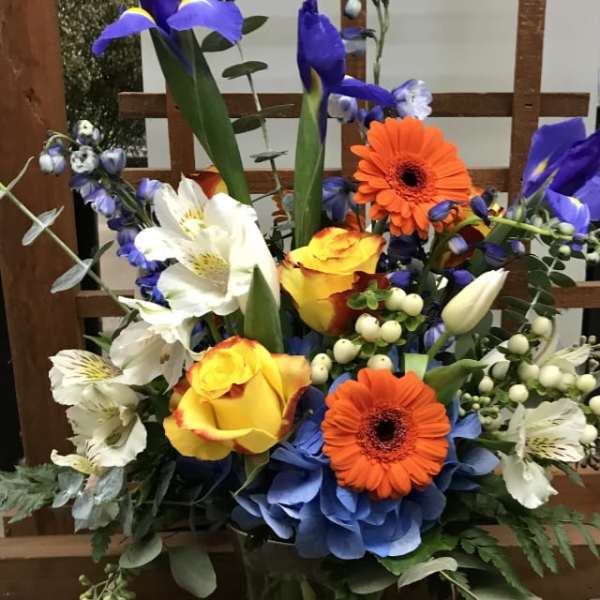 Colorful mixed bouquet in a glass vase with blue irises and orange gerbera daisies