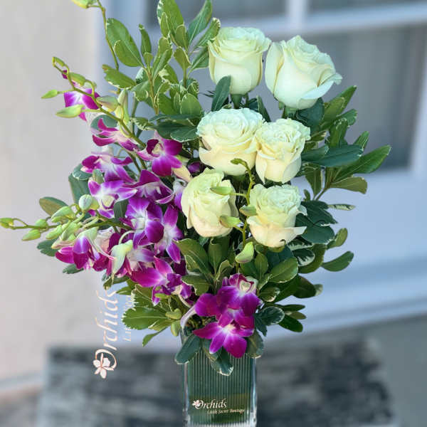 White roses and purple orchids arranged in a clear glass vase