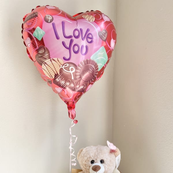 Heart-shaped balloon above a teddy bear in a pink gift box