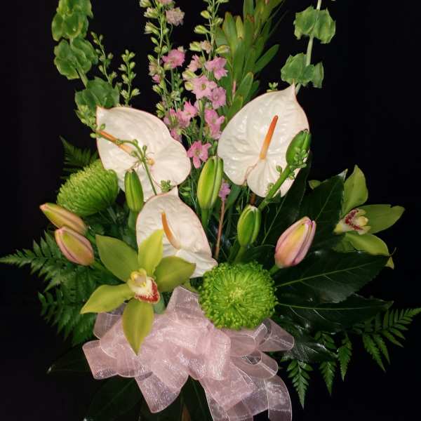 White anthuriums and pink orchids in a glass vase with a pink bow