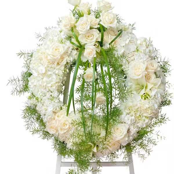 White rose and hydrangea wreath with green ribbon on a stand