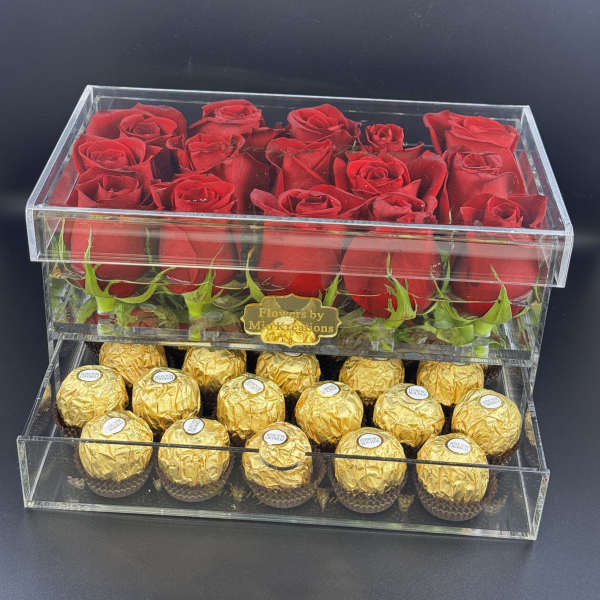 Red roses in a clear acrylic box above gold-wrapped chocolates