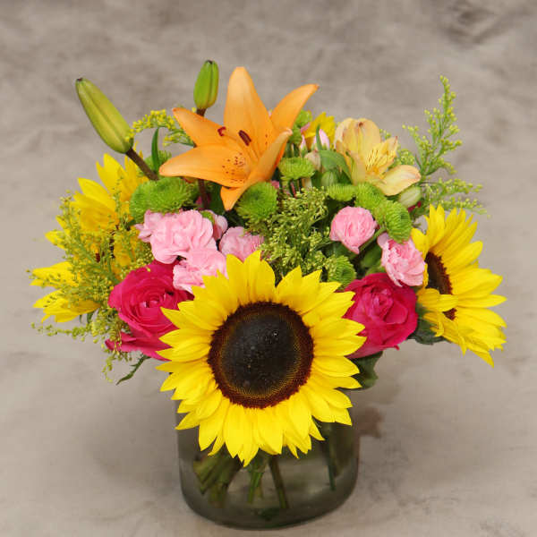 Mixed bouquet with sunflowers, lilies, roses, and carnations in a glass vase