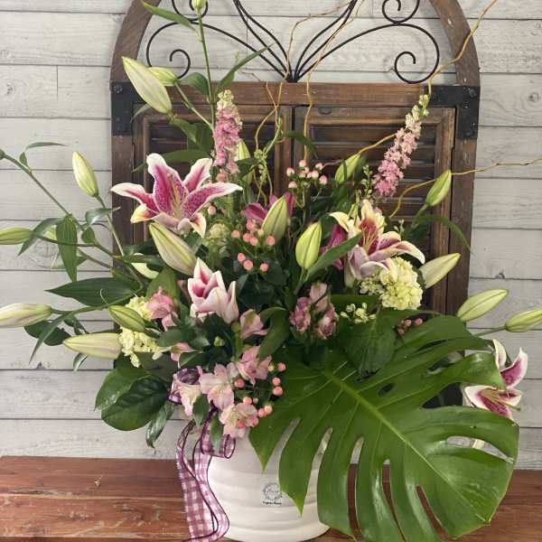 Pink and white lilies arranged in a white vase with a plaid ribbon.