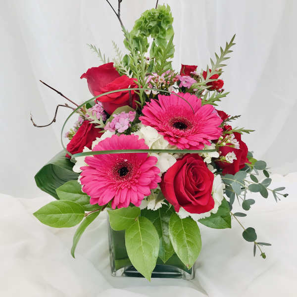 Pink gerbera daisies and red roses arranged in a glass vase