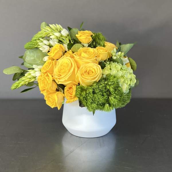 Yellow roses and green blooms arranged in a white vase
