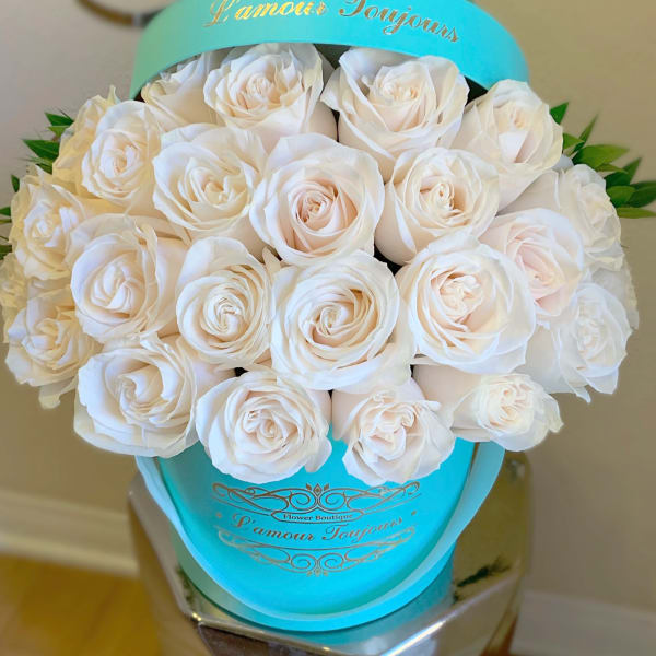 White roses arranged in a turquoise hatbox with gold lettering.