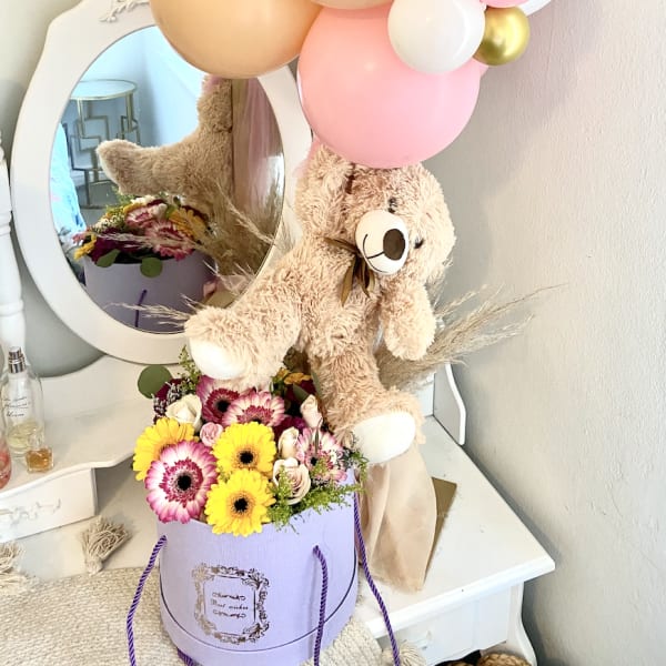Teddy bear with pastel balloons and a flower box arrangement