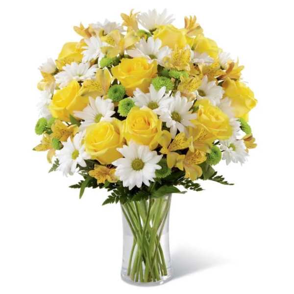 Yellow roses, white daisies, and green button mums arranged in a clear glass vase