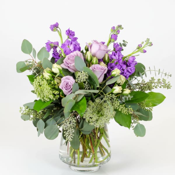 Lavender roses and purple flowers in a clear glass vase