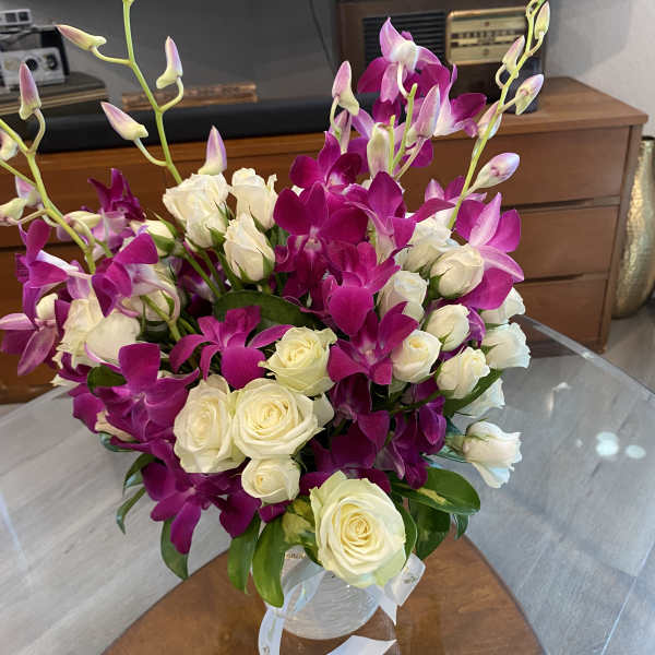 Bouquet of white roses and magenta orchids in a clear vase