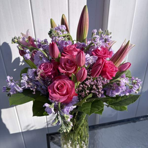 Pink roses and lilies arranged in a clear glass vase with lavender flowers