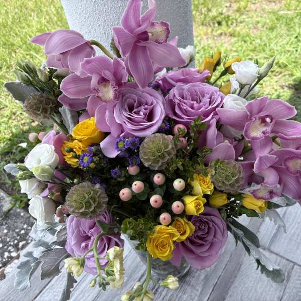 Bouquet of pink orchids, lavender roses, and yellow spray roses in a vase