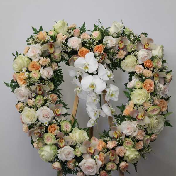 Heart-shaped floral wreath on an easel with white orchids and pastel roses