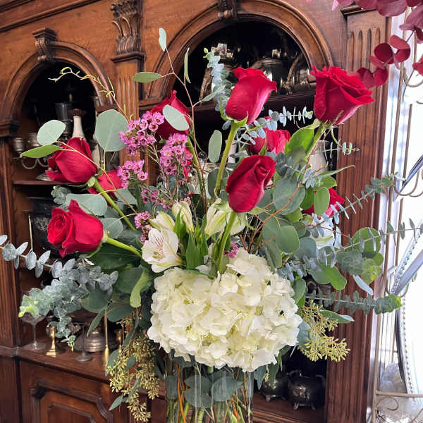 Tall bouquet of red roses, white hydrangea, and eucalyptus in a glass vase