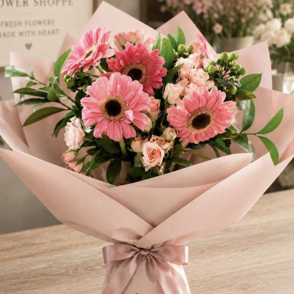Pink gerbera daisy and rose bouquet wrapped in blush paper with a ribbon