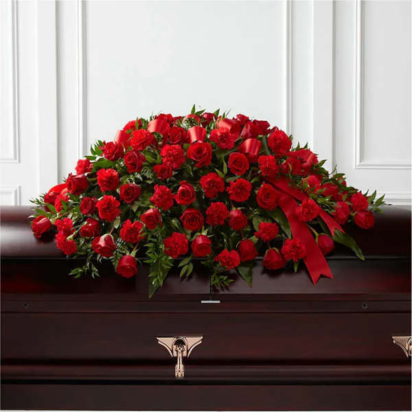 Red rose and carnation casket spray with ribbon on a dark wood casket