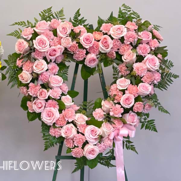 Heart-shaped pink rose and carnation wreath on a stand with a ribbon