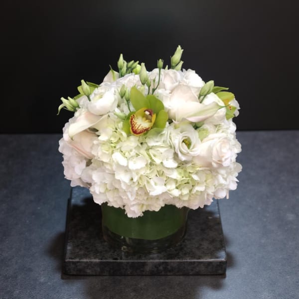White floral arrangement in a glass vase with green accents