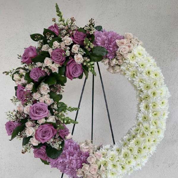 Large open wreath of purple and white flowers displayed on a black metal easel