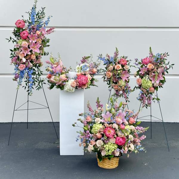 Large floral arrangements with pink, blue, and peach blooms in baskets and on stands