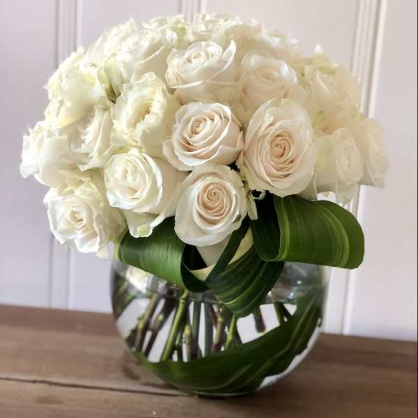 White rose bouquet in a clear glass vase with broad green leaves