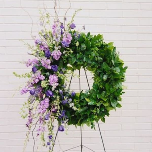 Large floral wreath with purple blooms and dense green foliage on a stand