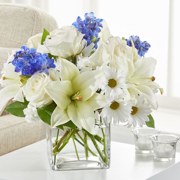 White lilies, roses, and daisies with blue flowers in a glass vase