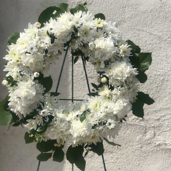 White floral wreath on a stand with dark green leaves