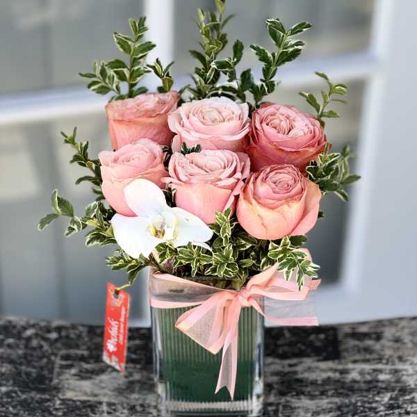 Pink roses in a glass vase with a white orchid and ribbon