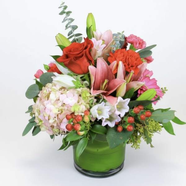 Mixed bouquet in a green glass vase with roses, lilies, hydrangea, and carnations