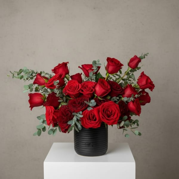 Red roses arranged in a black vase with eucalyptus accents