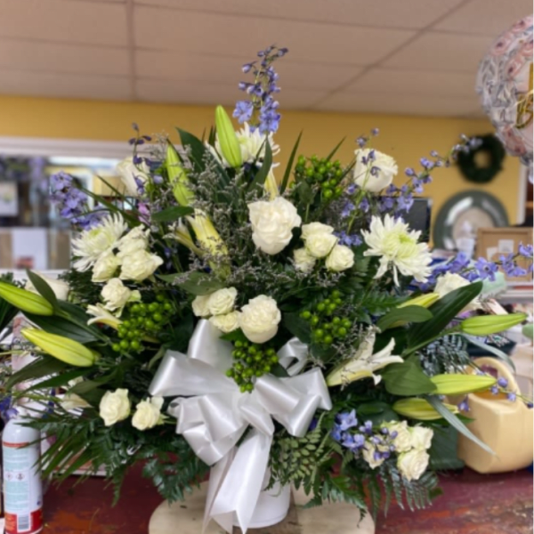White and blue floral arrangement in a white vase with a silver bow