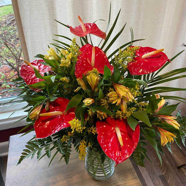 Red anthuriums and yellow flowers in a glass vase