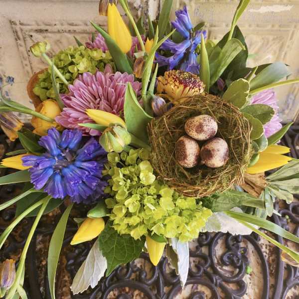 Mixed bouquet with purple and pink flowers, yellow tulips, and a bird nest centerpiece