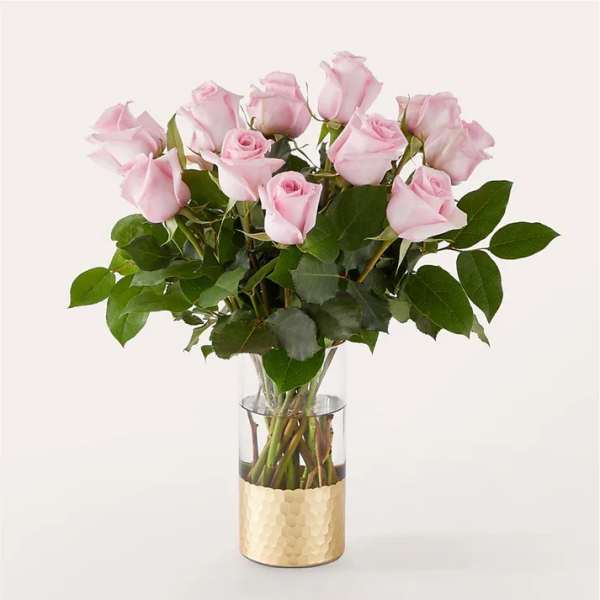 Pink roses arranged in a clear glass vase with a gold base