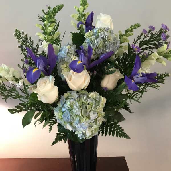 White roses and blue hydrangeas with purple irises in a tall vase