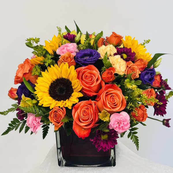 Mixed bouquet with sunflowers, roses, and carnations in a dark vase