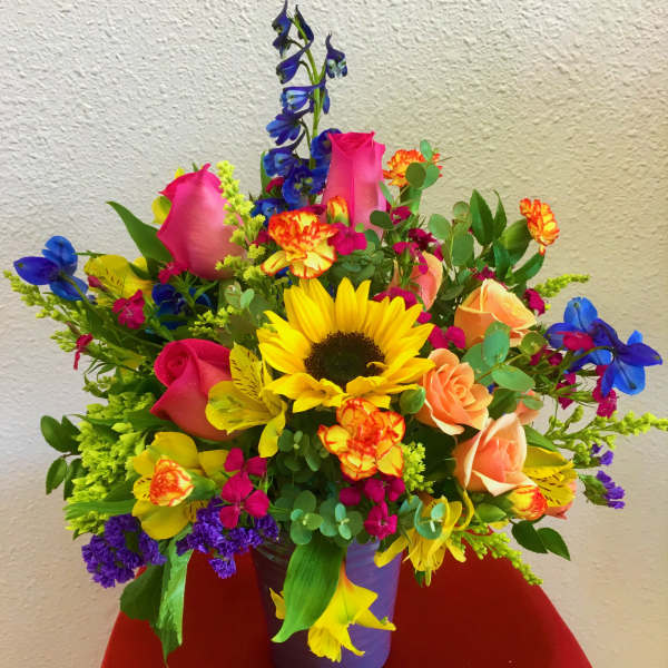 Colorful mixed bouquet in a purple vase with sunflowers and roses