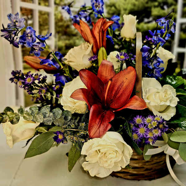 Basket arrangement of white roses, blue flowers, and red lilies