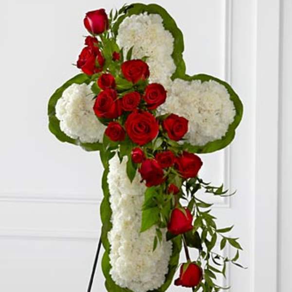 Cross-shaped floral tribute with red roses and white flowers on a stand