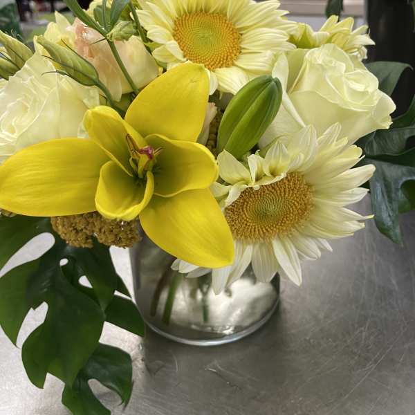 Yellow orchids, white roses, and pale daisies in a glass vase